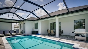 A swimming pool with lounge chairs and a grill area, enclosed by a glass roof structure. - 290) Perfect for Families! (Cape Coral)
