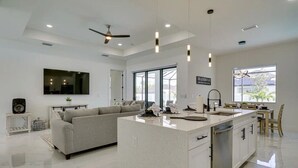 A modern kitchen with a central island, a dining area, and a living space with a sofa and TV. - 290) Perfect for Families! (Cape Coral)