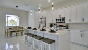 A modern kitchen with white cabinets, a central island with bar stools, stainless steel appliances, and pendant lighting. - 290) Perfect for Families! (Cape Coral)
