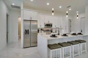 Una cocina moderna con armarios blancos, electrodomésticos de acero inoxidable y taburetes de bar.