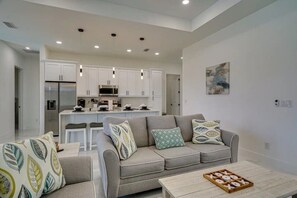Una sala de estar moderna con un sofá gris, una mesita de centro y una cocina al fondo.