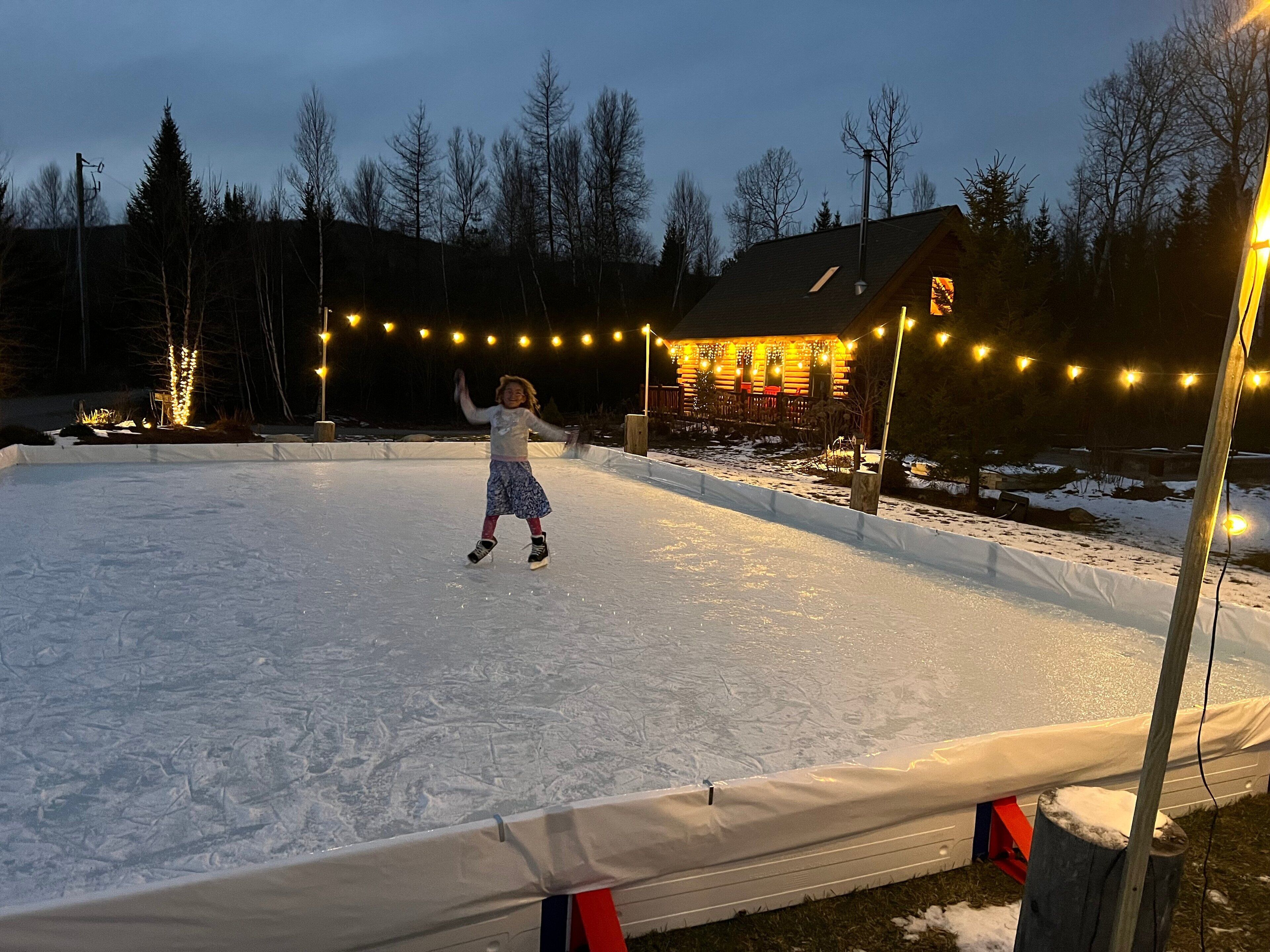 Un niño patina sobre hielo en una superficie nevada, con luces colgantes al fondo.
