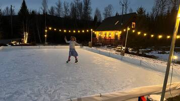 Un niño patina sobre hielo en una superficie nevada, con luces colgantes al fondo.