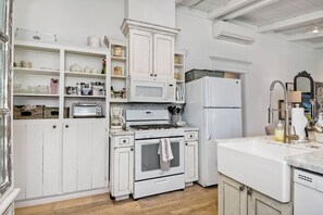 Una cocina con armarios blancos, estufa, microondas y refrigerador.