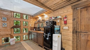 A rustic wooden cabin with a kitchen featuring a black refrigerator, a water dispenser, and a microwave. There are wooden cabinets and a small sink. - Amazonia (Rogers)