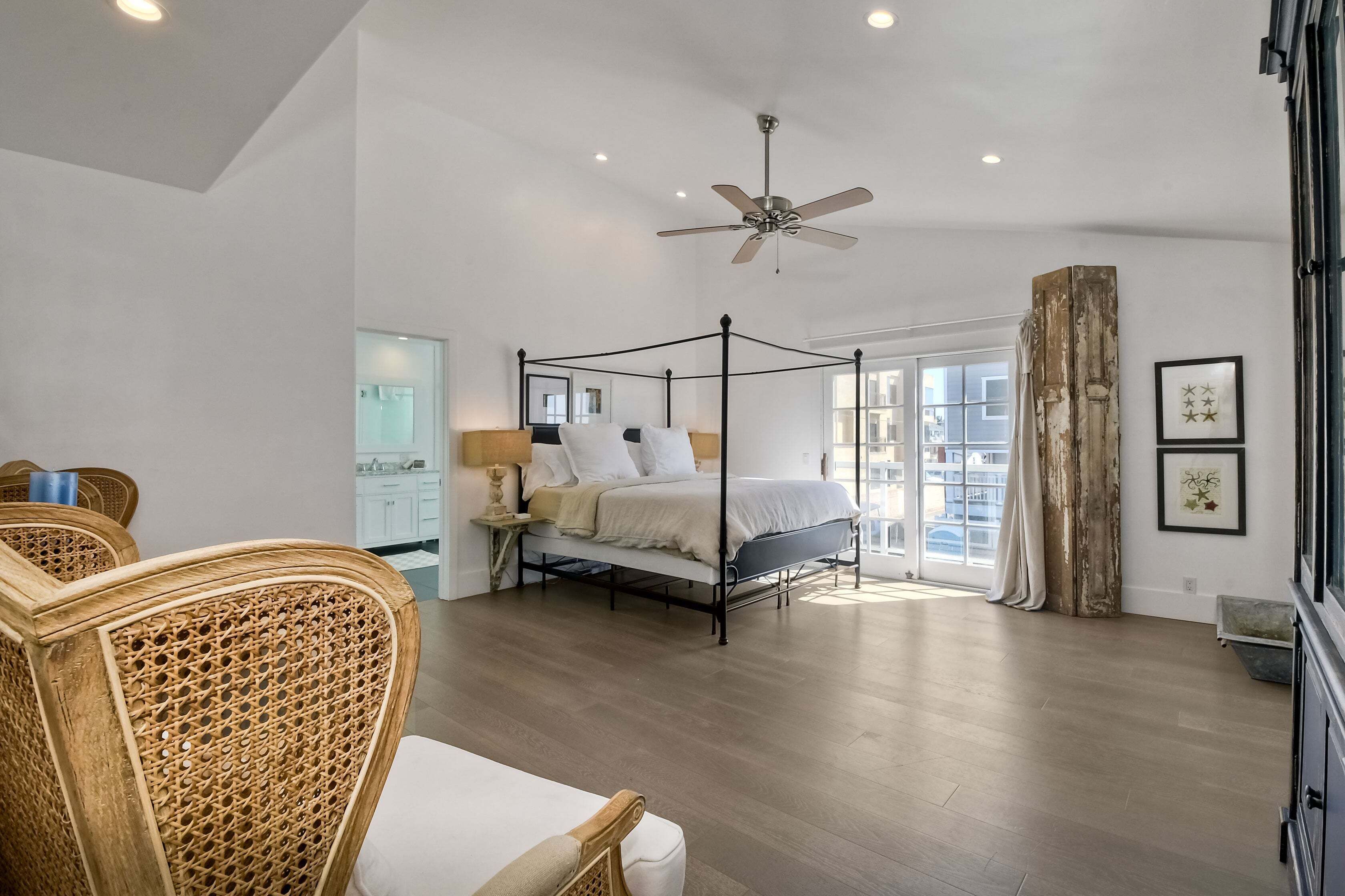 A spacious bedroom with a four-poster bed, a ceiling fan, and a large window.
