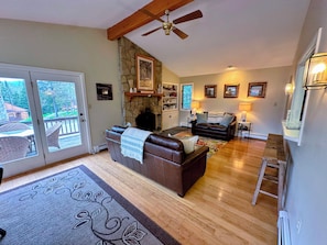A spacious living room with a fireplace, a ceiling fan, and a view through glass doors to an outdoor deck. - Fc39 Entry Level Bretton Woods Cottage on Beginner ski Trail (Bretton Woods)