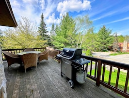 Una terraza de madera con mobiliario de mimbre y una parrilla.
