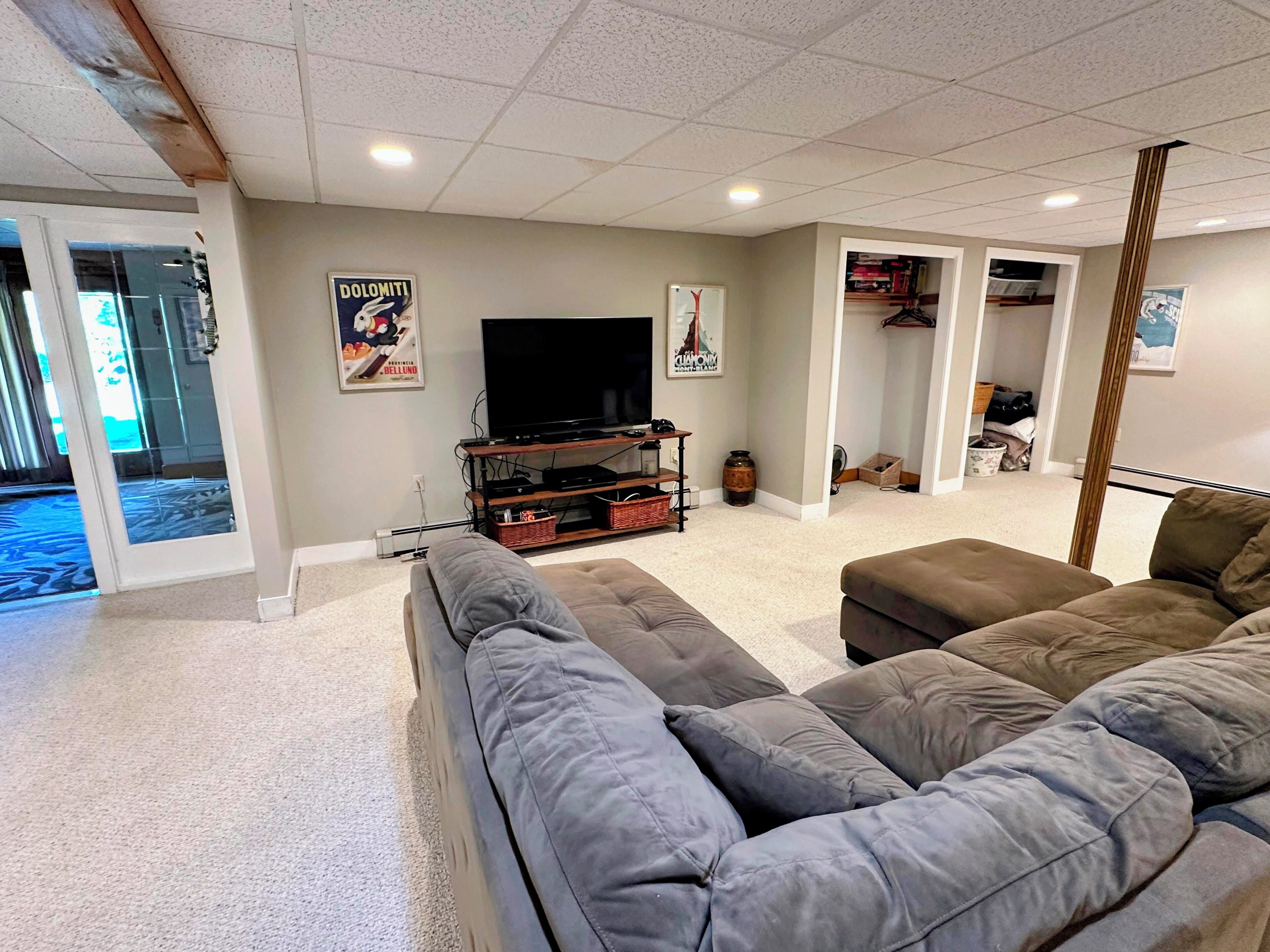 A living room with a grey sofa, a TV on a wooden stand, and a door leading to a hallway.