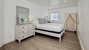 Une chambre à coucher avec un lit, une commode, un miroir et une fenêtre.