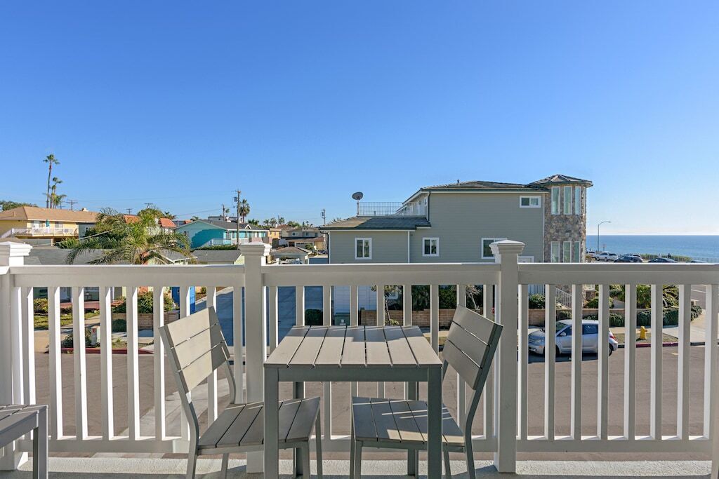 A balcony with a table and chairs, overlooking a beach and residential buildings.