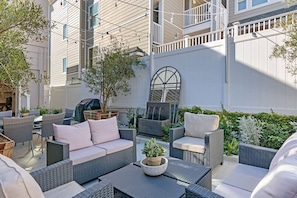 An outdoor patio with wicker furniture, a grill, and a large window. - 3690 Carlsbad Boulevard - Unit C (Carlsbad)