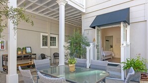 A covered patio with a glass table and wicker chairs, surrounded by potted plants and a white column. - 3690 Carlsbad Boulevard - Unit C (Carlsbad)
