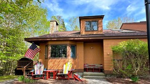 Una casa de madera con chimenea, un porche con sillas Adirondack y una bandera estadounidense.