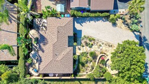 Luchtbeeld van een pand met een verharde oprit, een overdekt terras en een aangelegde tuin met diverse planten en een kronkelend pad.
