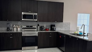 Une cuisine moderne avec des meubles de couleur sombre, des appareils électroménagers en acier inoxydable et un sol en marbre.
