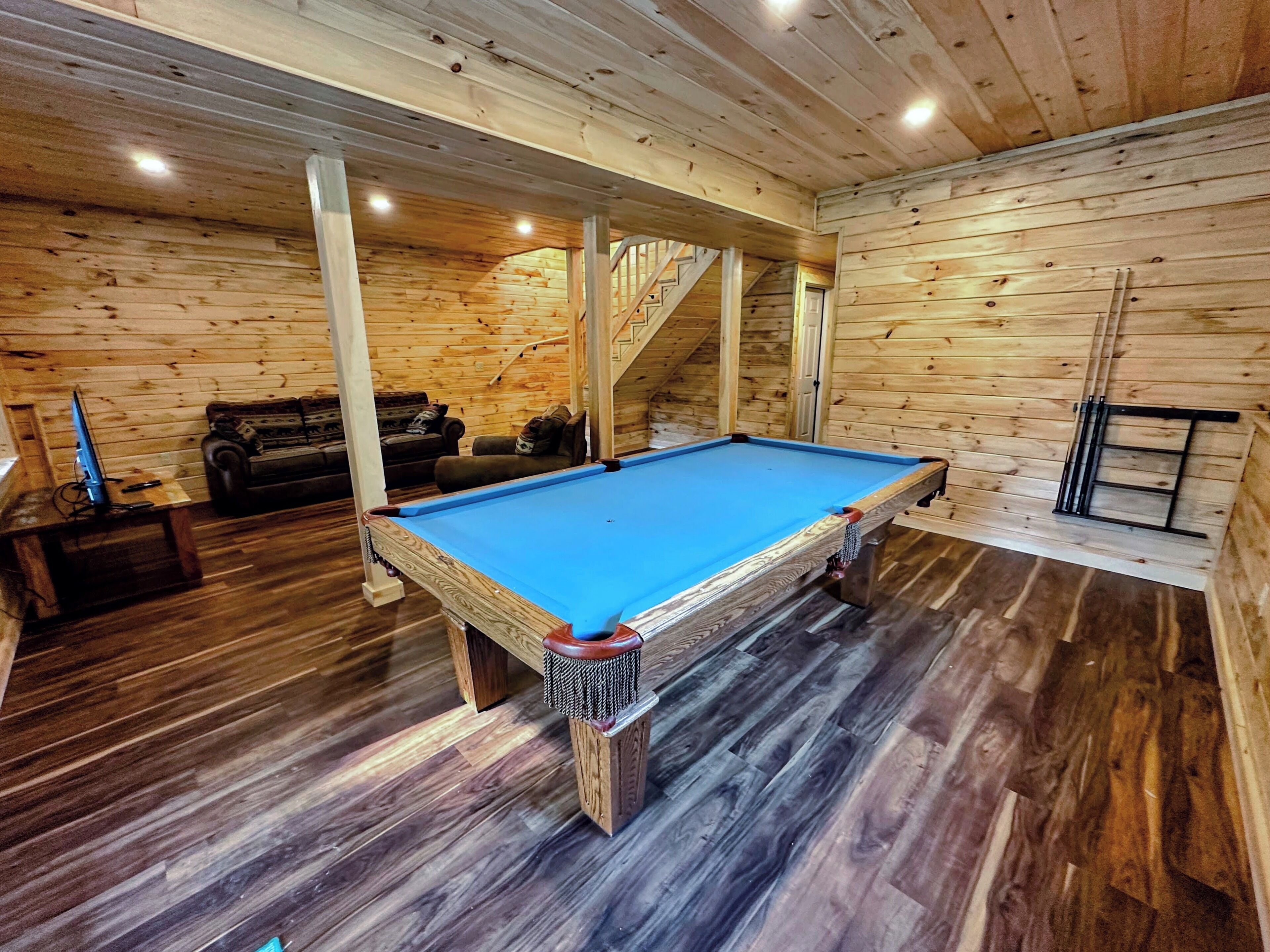 A pool table in a wooden room with a staircase and a couch.