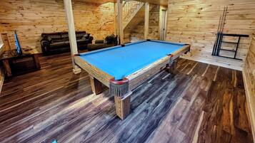 A pool table in a wooden room with a staircase and a couch.