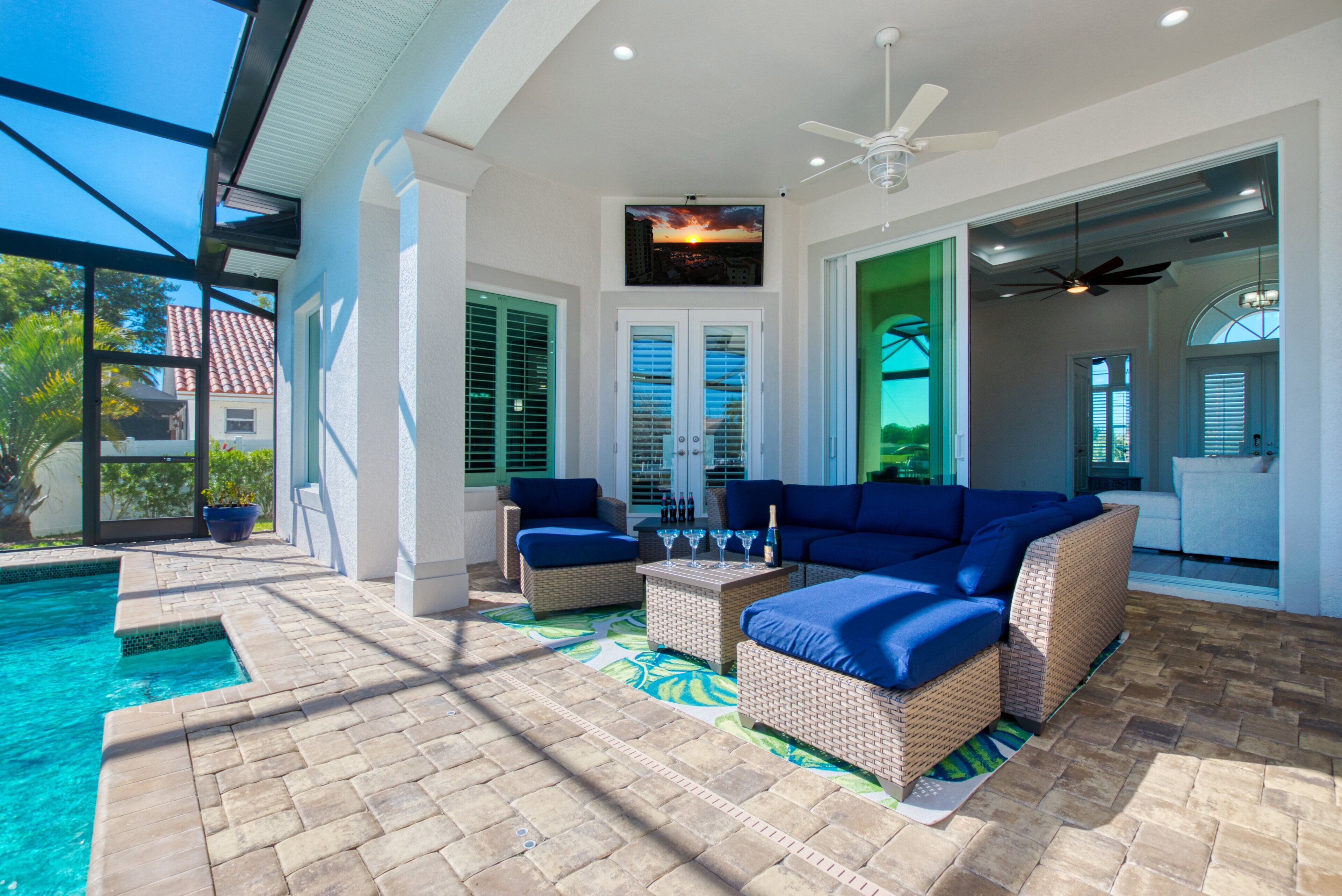 A poolside area with a wicker sofa, a table with glasses, and a ceiling fan.