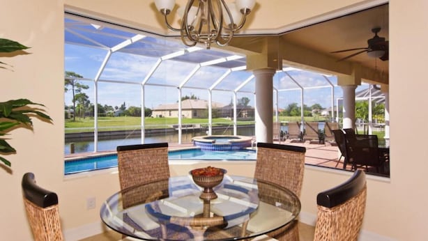 Un espace repas avec une table en verre et des chaises en osier, donnant sur une piscine et un coin salon extérieur.