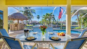 A dining area with a table set for two, overlooking a pool and palm trees. - Villa Viscaya (Cape Coral)