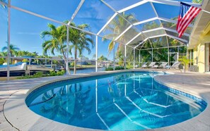 A swimming pool with a clear blue water, surrounded by a glass enclosure, palm trees, and a flag. - Villa Viscaya (Cape Coral)