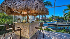 An outdoor bar area with a thatched roof, a pool, and chairs. - Villa Viscaya (Cape Coral)