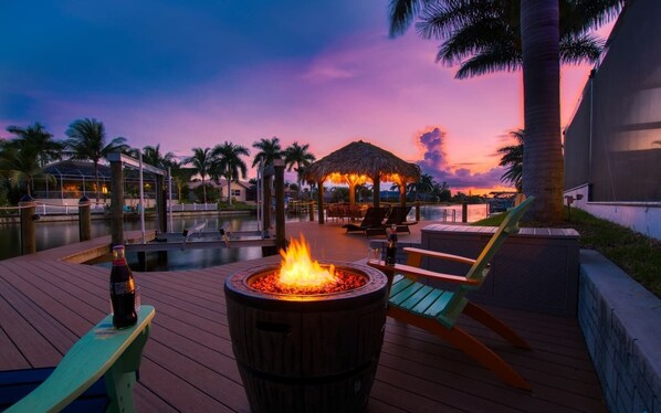 A wooden deck with a fire pit, lounge chairs, and a thatched-roof structure. - Villa Salt Life (Cape Coral)