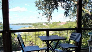A covered outdoor seating area with two chairs and a table, overlooking a scenic view of a body of water and greenery. - Shore Nuff, a Relaxing 4-bedroom Vacation Home on Canyon Lake (Canyon Lake)