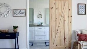 A room with a white dresser, a black side table, a wooden door, and a framed picture on the wall. - Shore Nuff, a Relaxing 4-bedroom Vacation Home on Canyon Lake (Canyon Lake)