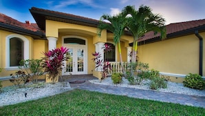 A yellow building with a tiled roof, a front door, and a small garden with various plants. - Villa Sunset View (Cape Coral)