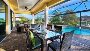 A covered outdoor dining area with a glass table and wicker chairs, overlooking a swimming pool. - Villa Sunset View (Cape Coral)