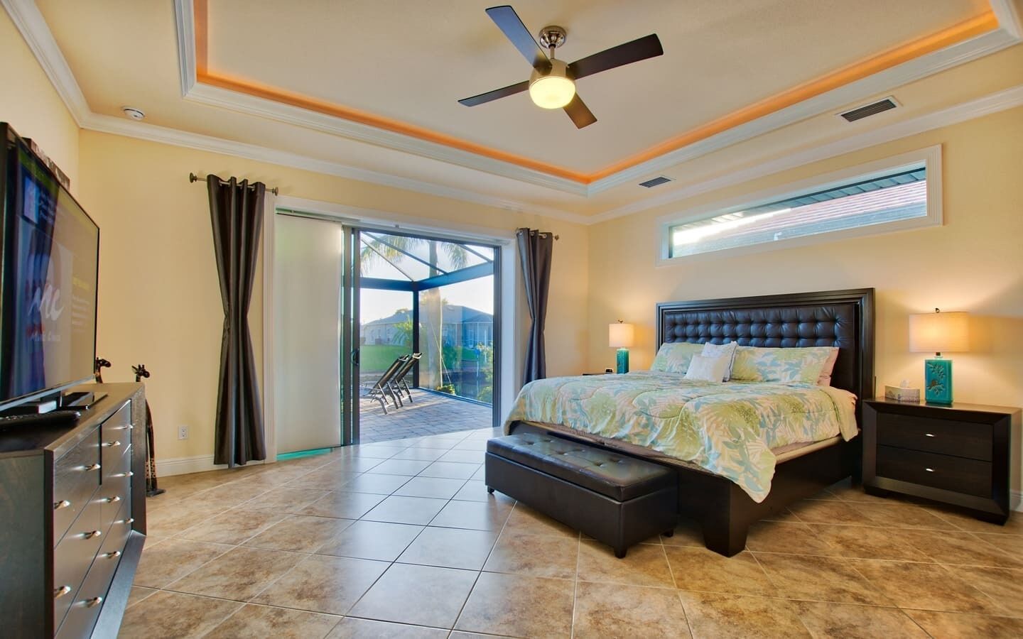 Ein geräumiges Schlafzimmer mit einem großen Bett, einem Deckenventilator und Blick ins Freie durch eine Schiebetür.