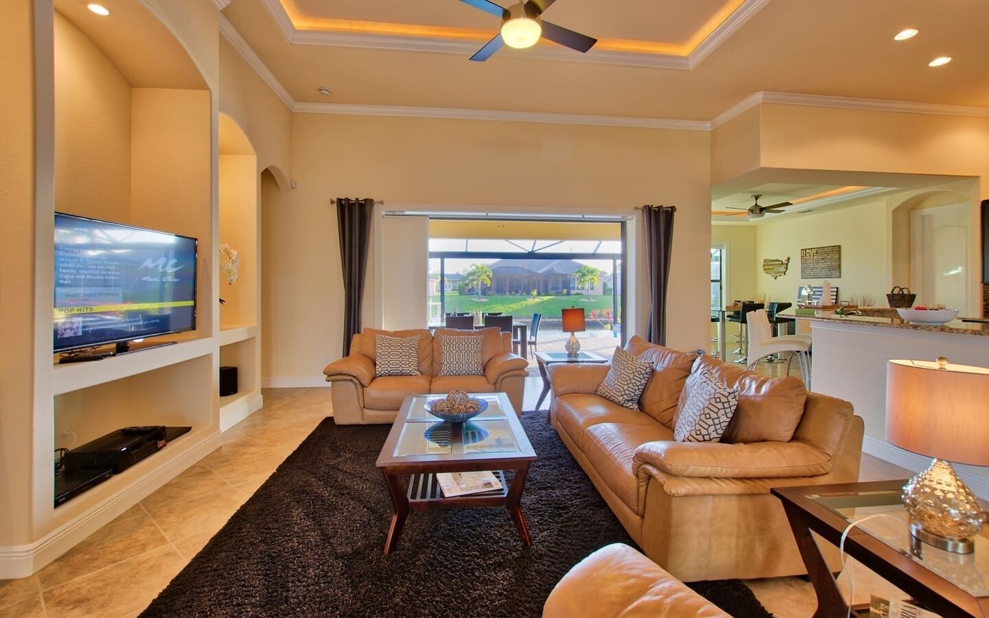 A spacious living room with a large flat-screen TV, leather sofas, a coffee table, and a view of the outdoors.