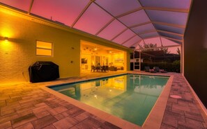 An indoor swimming pool with a covered patio area, a barbecue setup, and a view of the surrounding landscape. - Villa Little Diamond (Cape Coral)