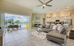 A spacious living room with a large sofa, a dining area with chairs, a kitchen with cabinets, and a view of a body of water through large windows. - Villa Little Diamond (Cape Coral)