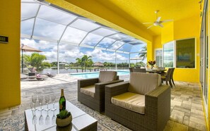 A covered outdoor seating area with wicker furniture, a pool, and a view of the landscape. - Villa Little Diamond (Cape Coral)