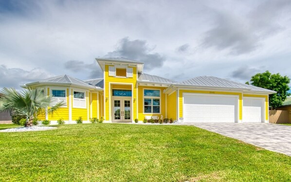 A yellow two-story house with a garage, a front porch, and a well-maintained lawn. - Villa Little Diamond (Cape Coral)