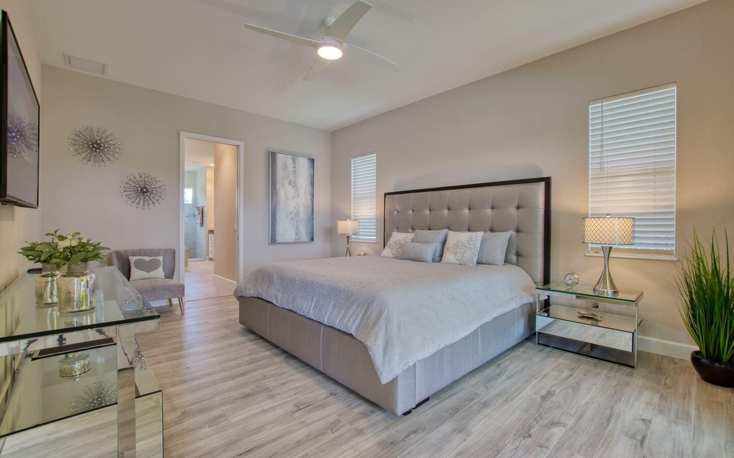 Un dormitorio moderno con una cama grande, una mesa de centro de vidrio, una silla y un ventilador de techo.
