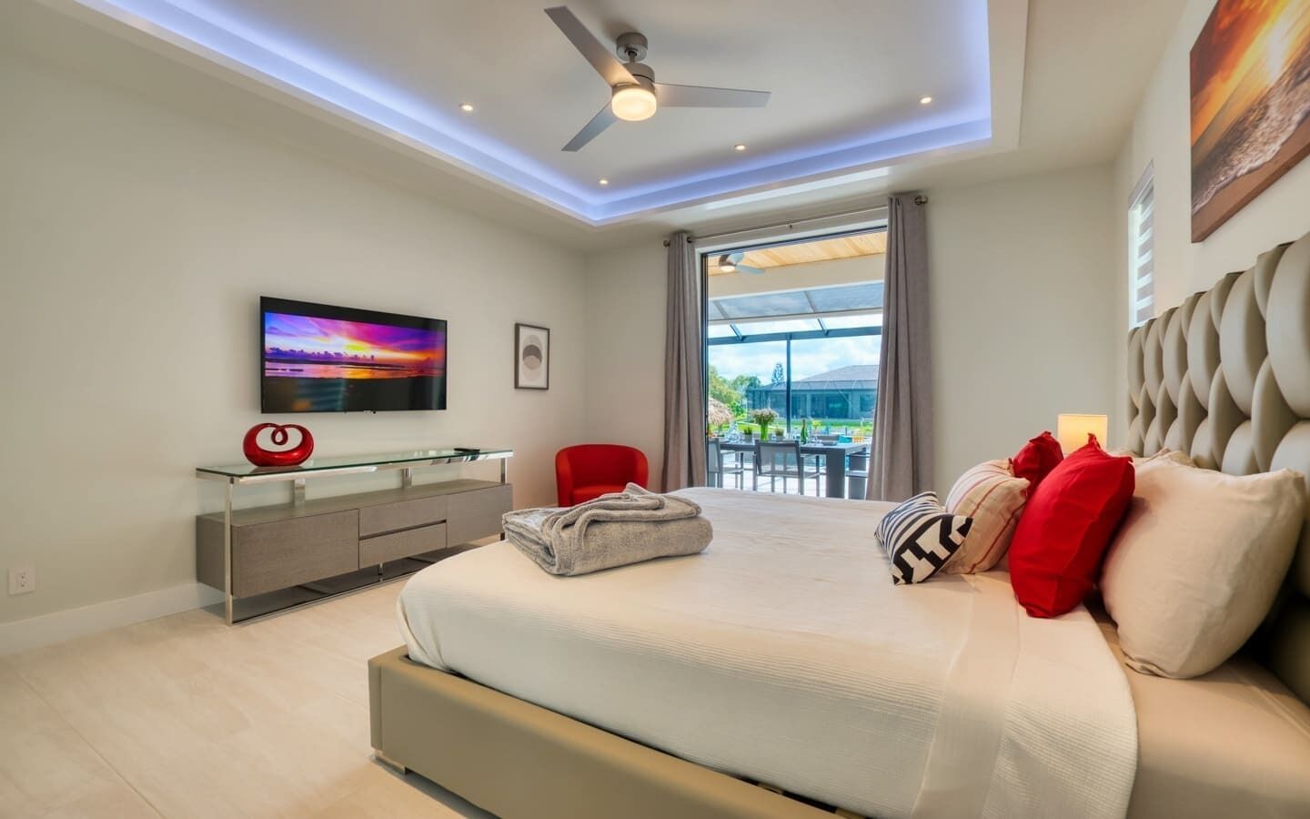 Ein modernes Schlafzimmer mit einem großen Bett, einem Fernseher auf einer Glasablage, einem roten Sessel und Blick ins Freie.