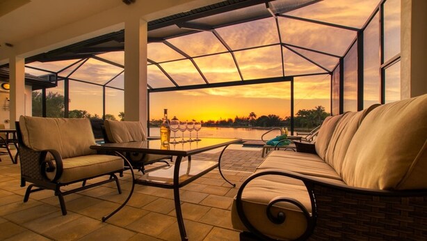 A spacious outdoor seating area with a glass enclosure, a table with wine glasses, and a bottle. - Villa Paradise (Cape Coral)