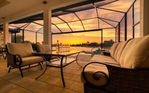 A spacious outdoor seating area with a glass enclosure, a table with wine glasses, and a bottle. - Villa Paradise (Cape Coral)