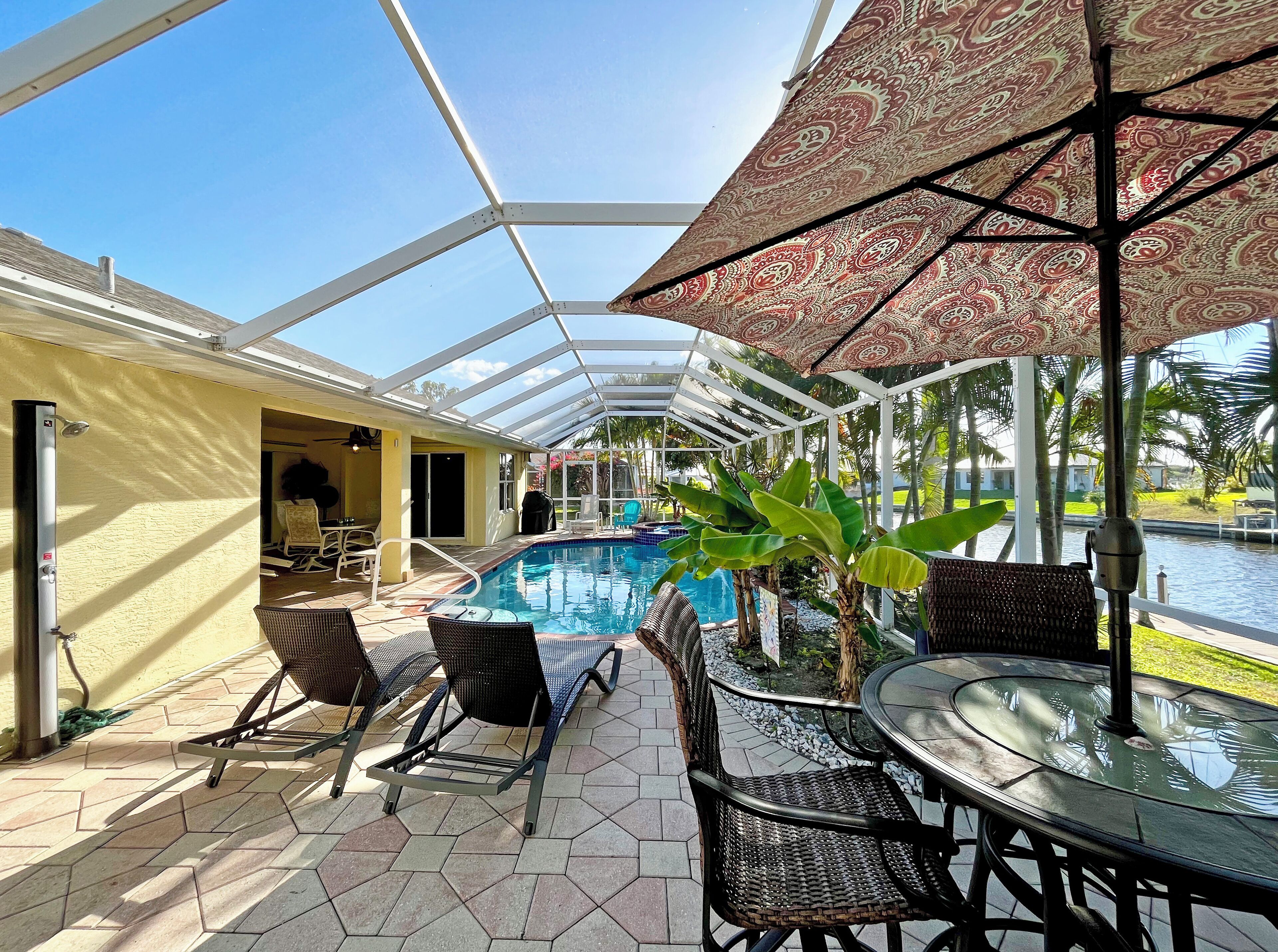 A covered outdoor area with a pool, lounge chairs, and umbrellas.