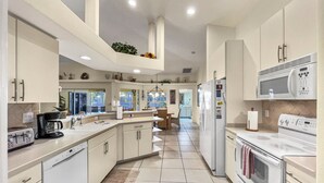 Una cucina moderna con mobili bianchi, un'isola centrale, un frigorifero, un forno a microonde e un piano cottura.