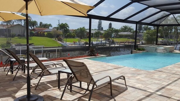 Piscina esterna coperta con lettini e ombrelloni, vista su una zona residenziale e un corpo d'acqua.
