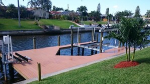 Un molo che si protende in uno specchio d'acqua, con una zona erbosa e una palma nelle vicinanze.