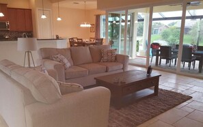 A living room with a sofa, coffee table, and a dining area with chairs and a table. - Villa Alani (Cape Coral)