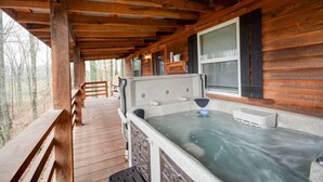 Une cabane en bois avec un bain à remous sur une terrasse en bois, entourée d’arbres.