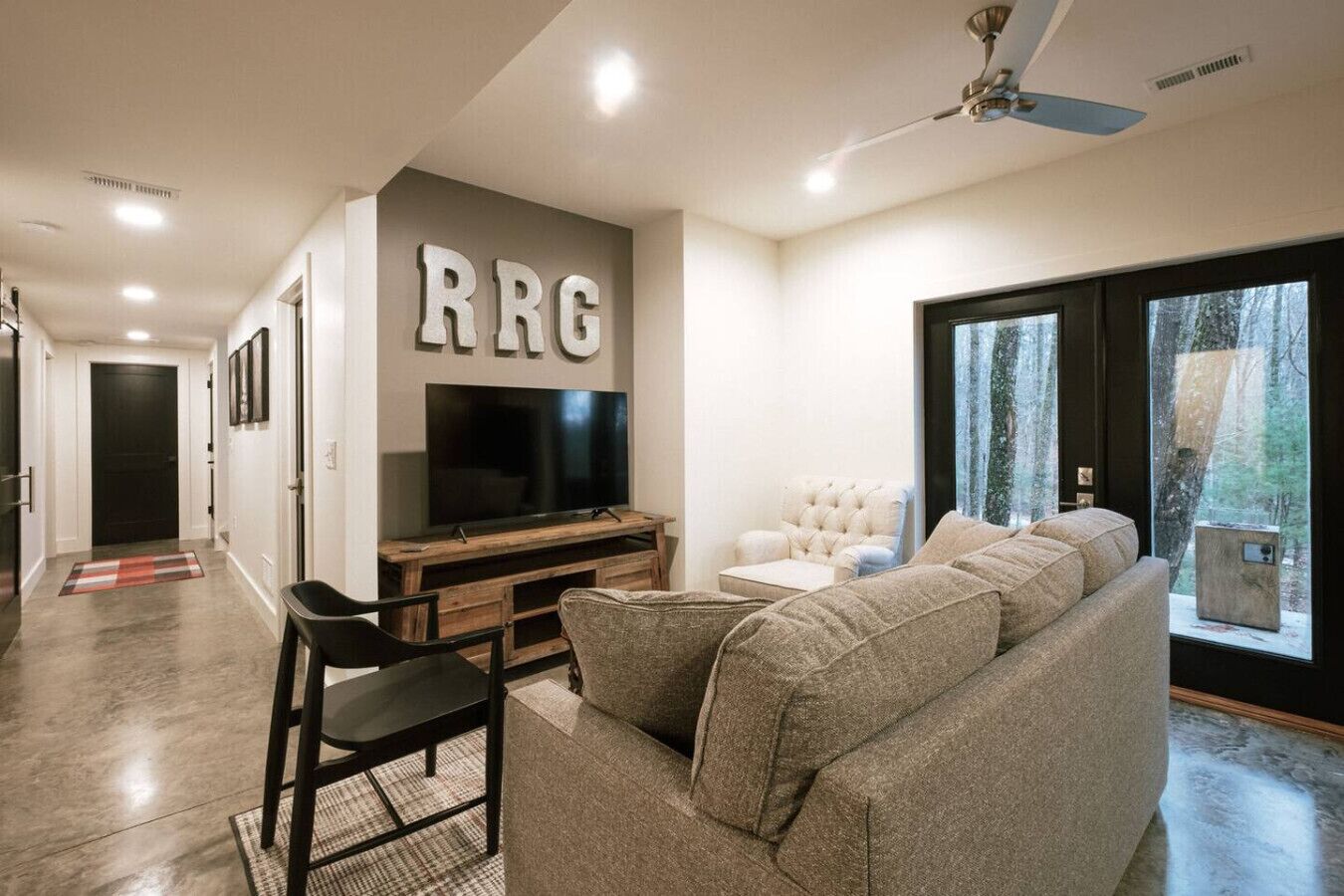A modern living room with a large flat-screen TV, a beige sofa, and a white armchair.