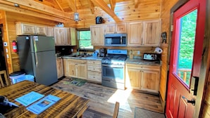 Eine Holzhütte mit einer Küche, inklusive Kühlschrank, Mikrowelle, Herd und Holzschränken.